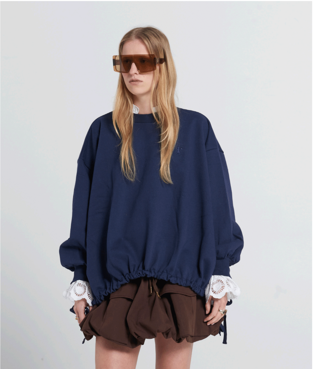 Person wearing a navy blue oversized sweater with lace trim and a brown skirt on a white background
