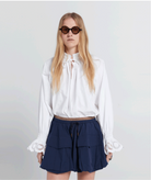 Woman wearing a white blouse and navy skirt with sunglasses on a plain background
