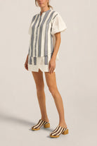 Woman wearing a striped shirt and shorts with striped shoes on a plain background