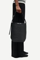 Person holding a black woven handbag with a visible brand logo on a white background