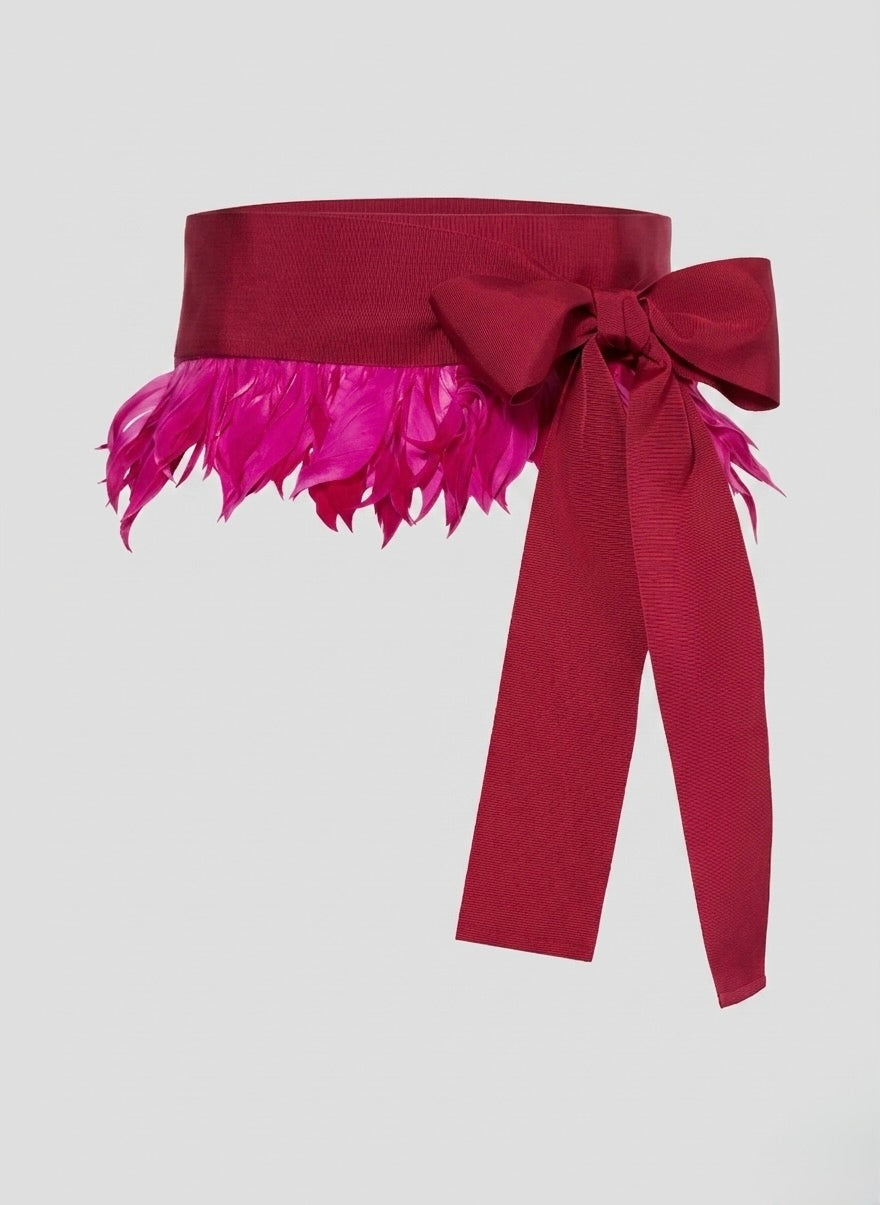 Red belt with a large bow and pink feathered trim on a light gray background