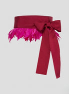 Red belt with a large bow and pink feathered trim on a light gray background