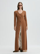 Woman wearing a long brown cardigan over a white dress on a light gray background
