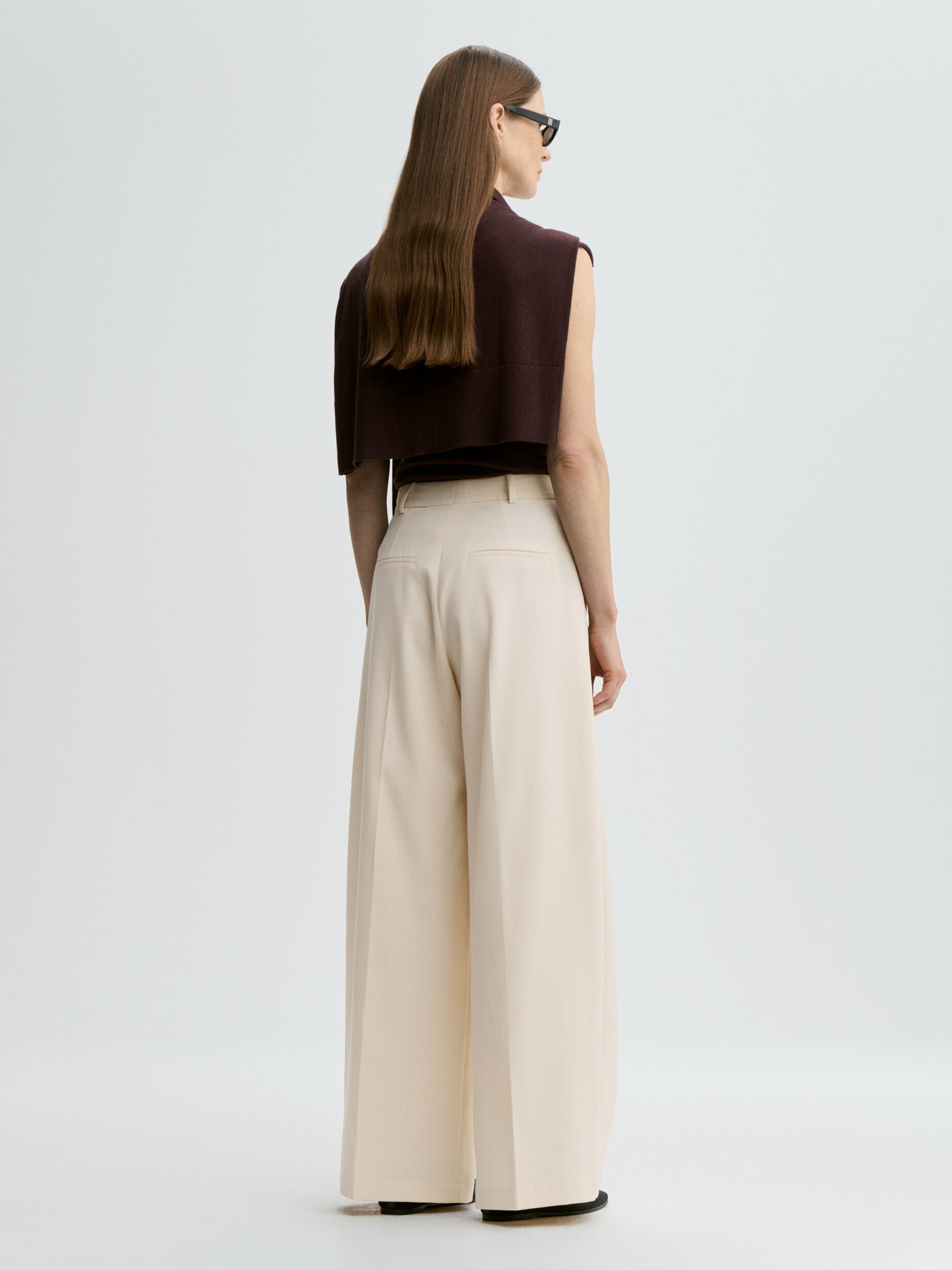 Woman wearing a brown top and beige wide-leg pants on a white background