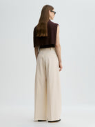 Woman wearing a brown top and beige wide-leg pants on a white background